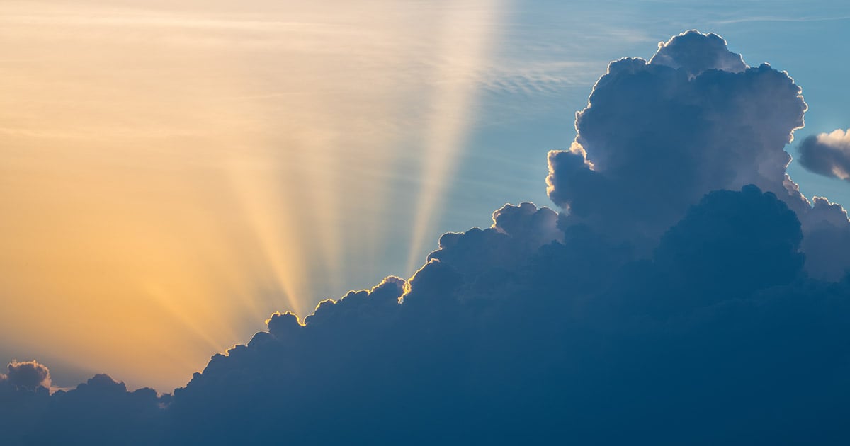 Sky with clouds shadowed in front with sunlight shining behind